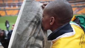 epa03984281 A supporter of late South African president Nelson Mandela kisses a portrait of Mandela prior to his memorial service at the First National Bank (FNB) Stadium, in Soweto, Johannesburg, South Africa, 10 December 2013. Nobel Peace Prize winner Nelson Mandela died at the age of 95 on 05 December 2013.  EPA/DAI KUROKAWA