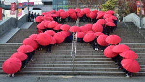 Gli studenti di Seoul, Sud Corea, disegnano il fiocco rosso, simbolo della lotta all'AIDS con degli ombrelli