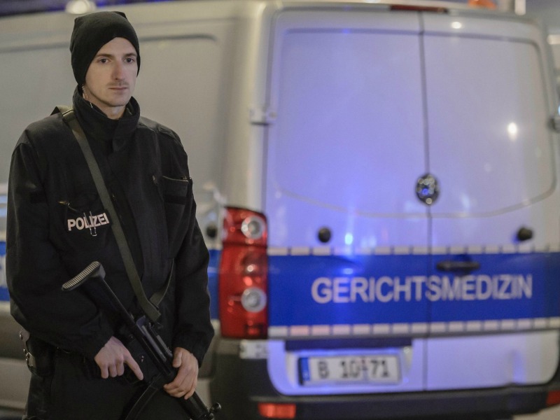 Un poliziotto armato davanti a una camionetta del dipartimento di medicina legale di Berlino. Foto Ansa